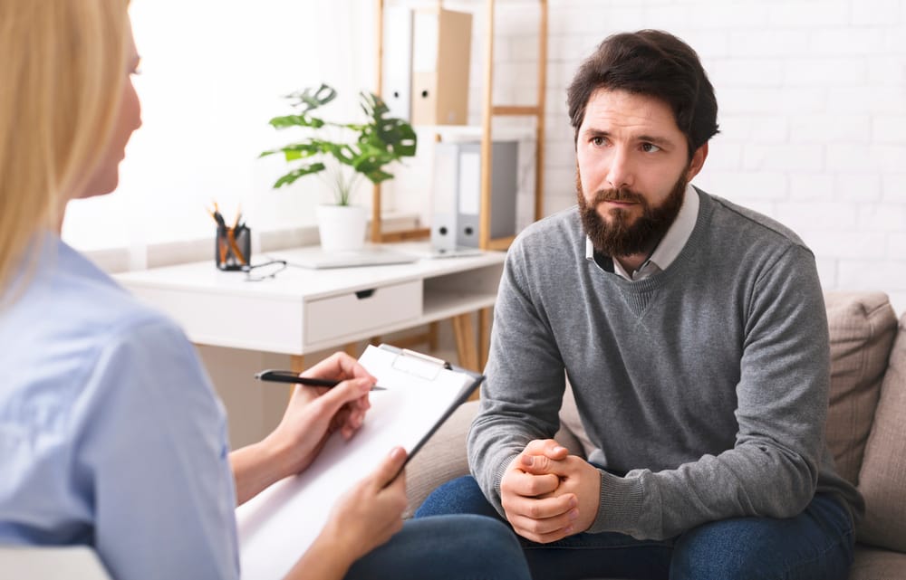Stressed young man talking to psychologist at therapy